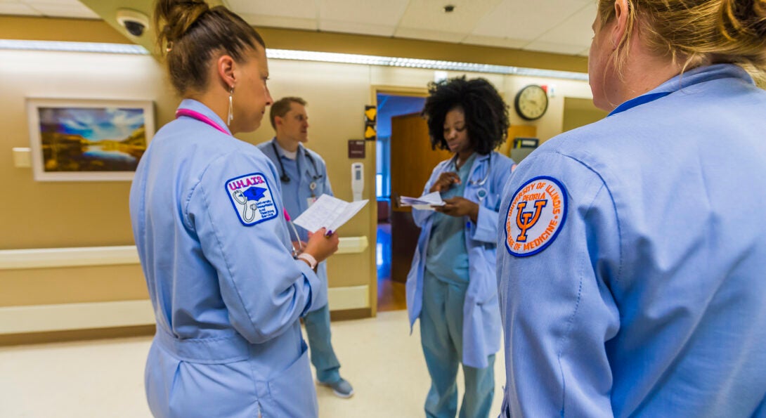 Residents stand in a hallway, reviewing medical records. On one arm a UICOMP patch is visible.