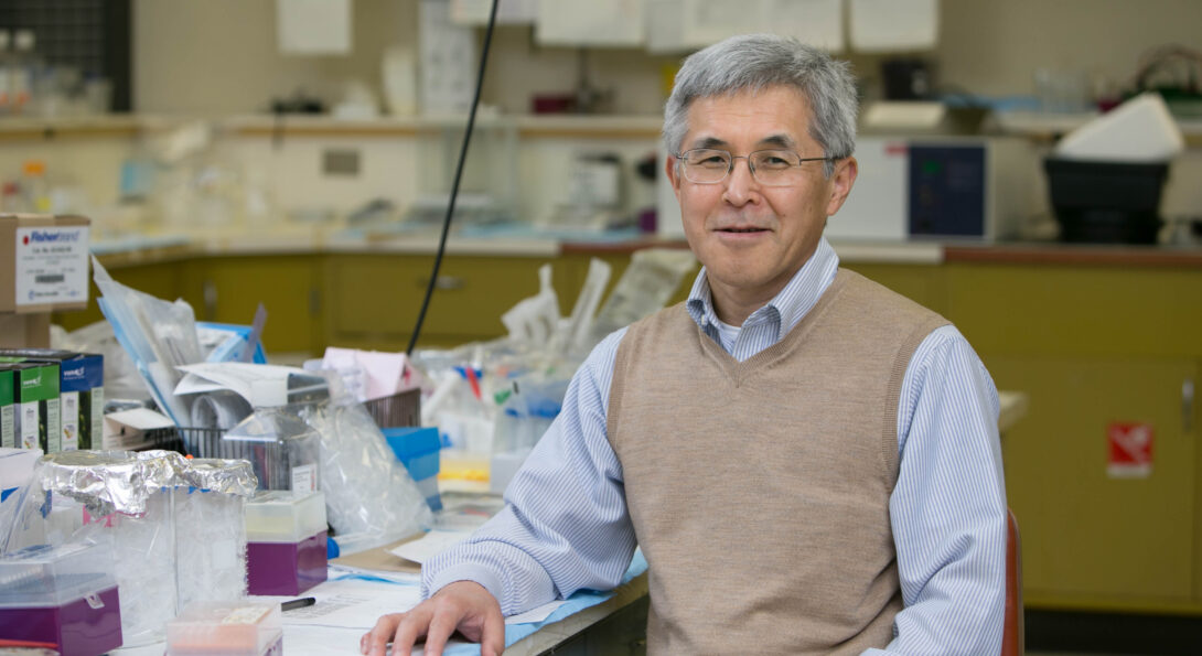 Dr. Fukuchi sits at a lab workspace and smiles for camera.
