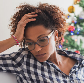 A depressed woman sits in front of a Christmas tree.
                  