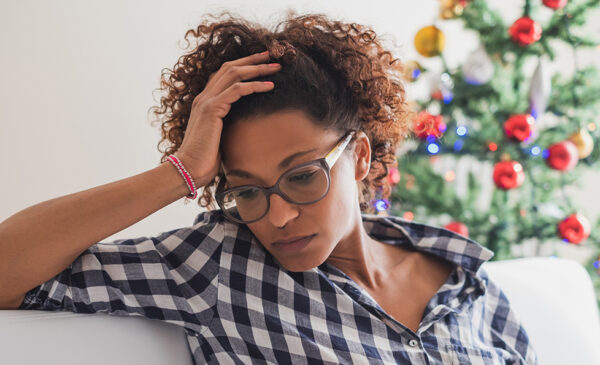 A depressed woman sits in front of a Christmas tree.